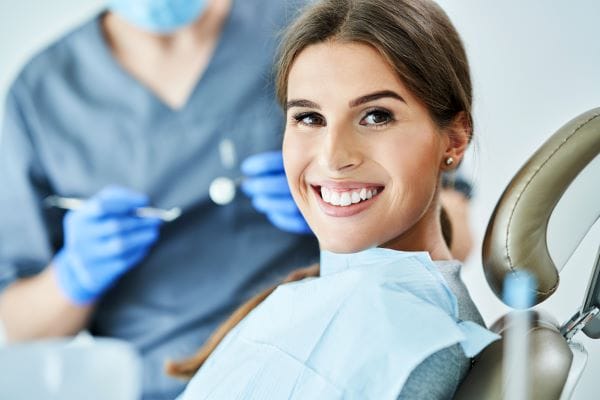 Patient smiling in dental chair during routine dental checkup with dentist in background.